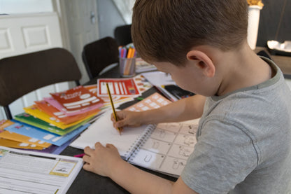 Overhead view of a child using a pencil to practice letter formation in a handwriting workbook with instructional examples.
