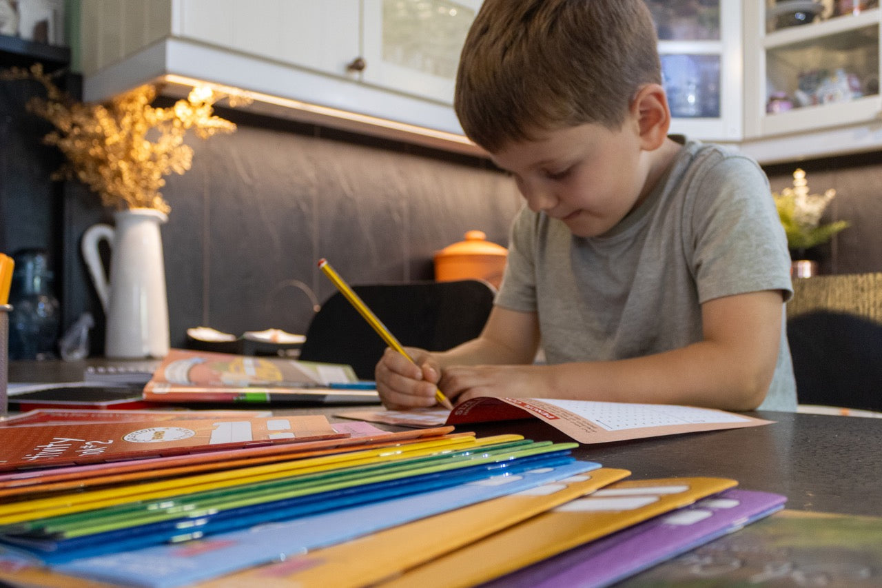 Young child concentrating while practicing handwriting with a pencil in an activity book at a table.