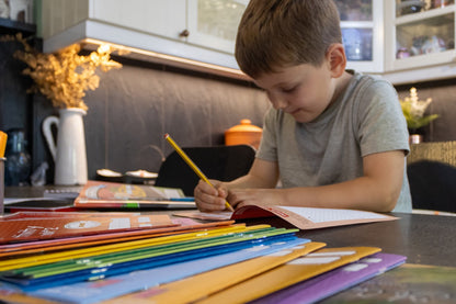 Young child concentrating while practicing handwriting with a pencil in an activity book at a table.