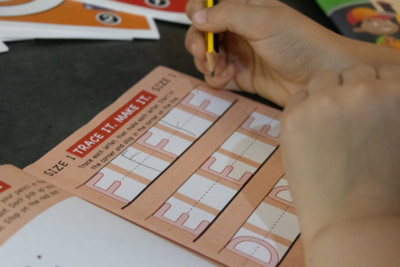 Close-up of a child tracing size one handwriting patterns with a pencil in a handwriting practice workbook.