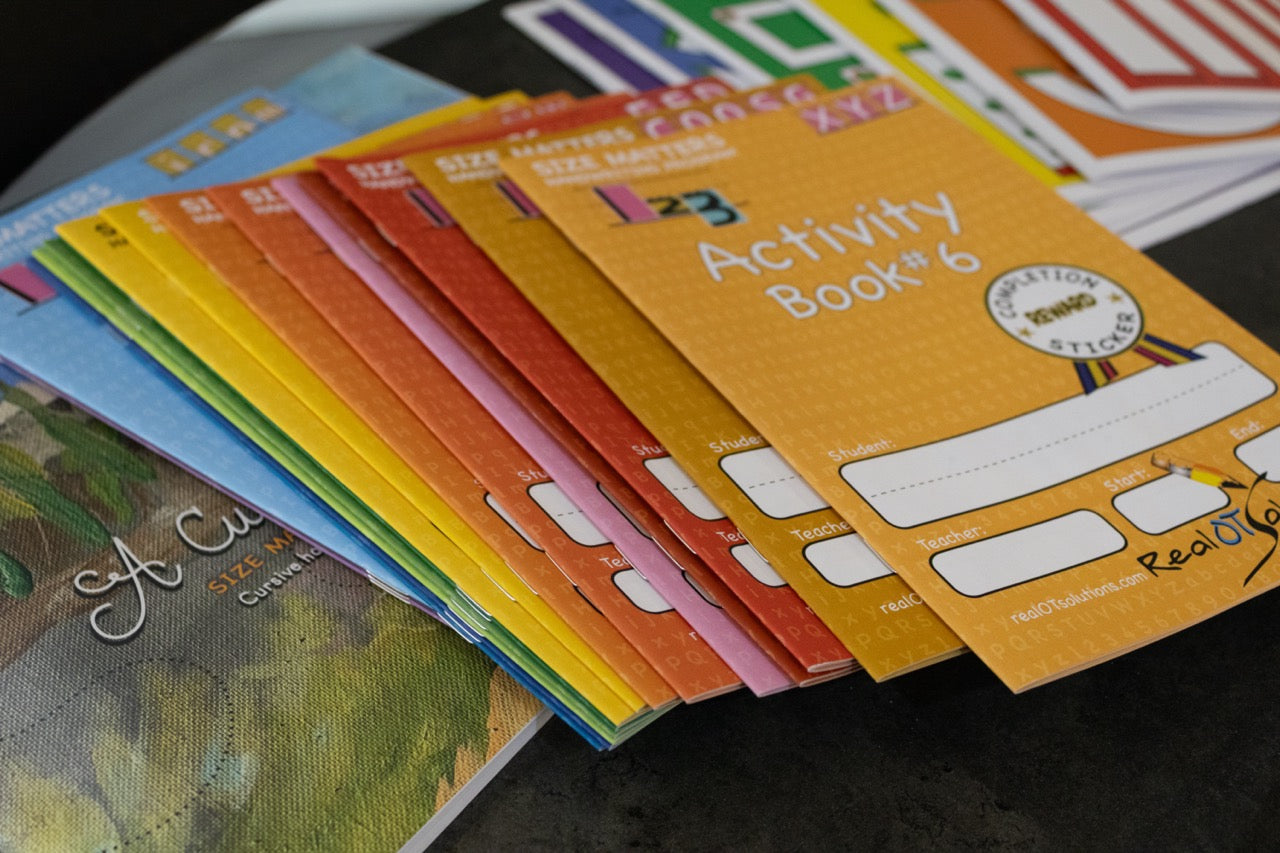 Stack of colorful handwriting activity books and learning materials arranged on a table for handwriting instruction and practice.
